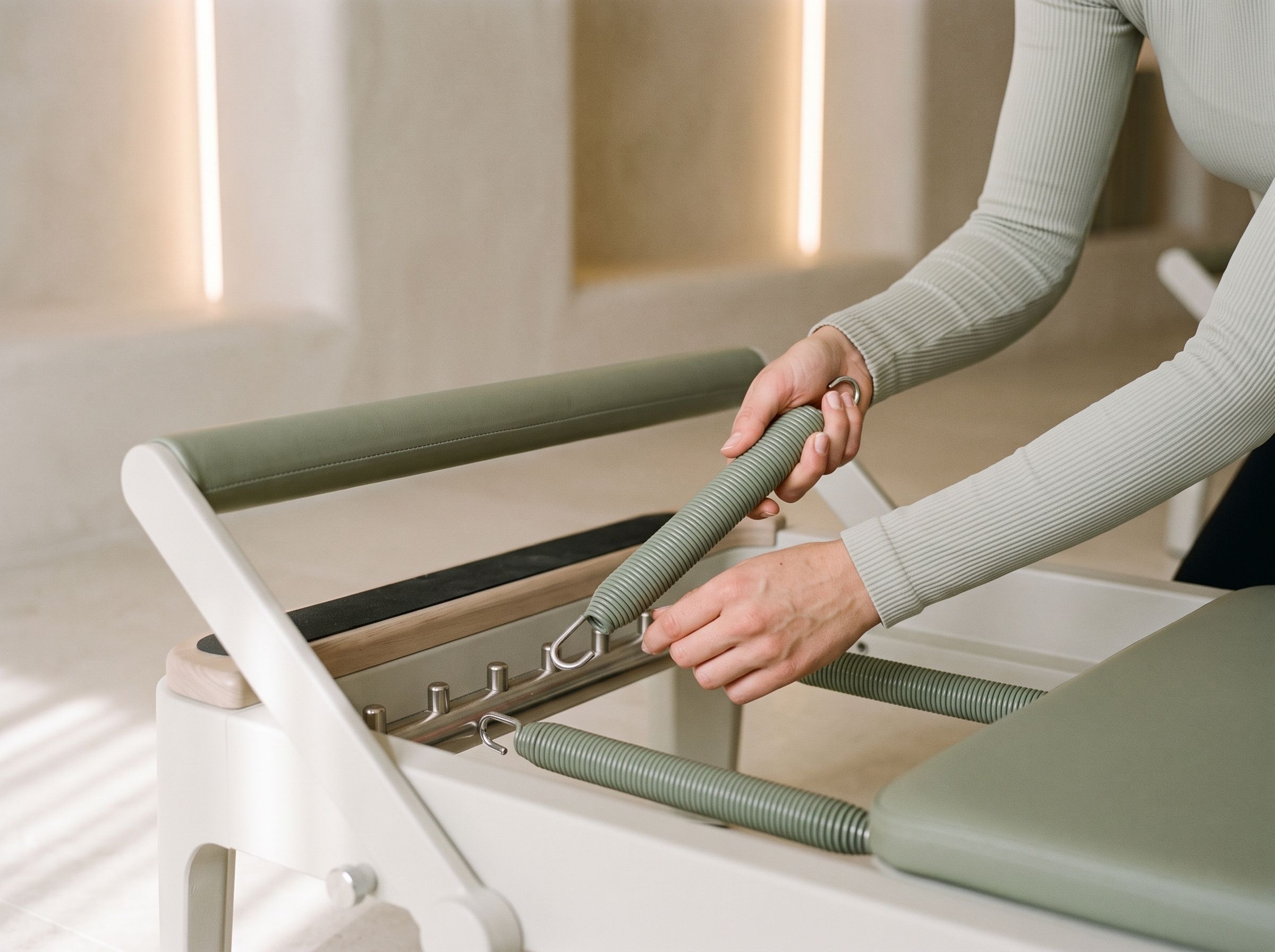 Close detail of hands in a sage sleeve hooking a sage spring onto the reformer’s spring bar.