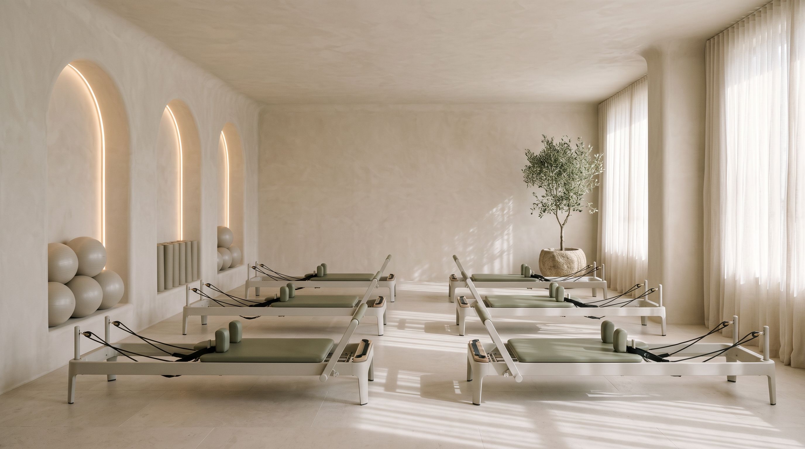 The Arch Room before class: limewash walls with three lit arched niches, reformers with sage upholstery, an olive tree and sheer linen curtains.
